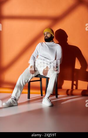 Ein stilvoller Mann in modischer Kleidung sitzt auf einem Stuhl neben einer lebendigen Wand. Stockfoto