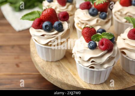 Leckere Cupcakes mit verschiedenen Beeren und Minze auf Holztisch, Nahaufnahme Stockfoto