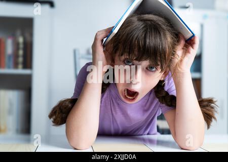 Das Mädchen langweilt sich, mit einem Buch auf dem Kopf zu lernen Stockfoto