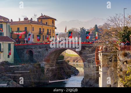 Ivrea, Italien - 19. Februar 2023: Blick auf die alte Brücke (Ponte Vecchio) während der Orangenschlacht mit Kämpfern und Menschenmengen. Historischer Karneval von Stockfoto