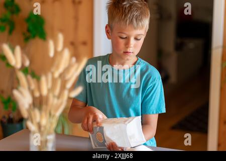 Junge, der Zucker aus einer Packung auf einer Küchenwaage wägt Stockfoto