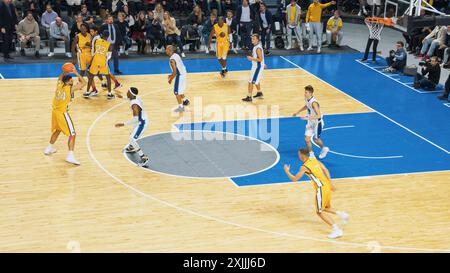 TV-Broadcast-ähnliche Aufnahmen von Basketball-Meisterschaften in einer Arena. Gelbes Team, das den Ball zwischen den Teamkollegen legt, wobei der Forward Spieler aus der Distanz ein 2-Punkte-Tor erzielen will. Sports Channel. Stockfoto