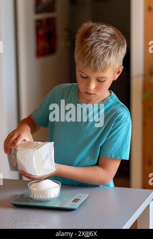 Junge, der Zucker aus einer Packung auf einer Küchenwaage wägt Stockfoto