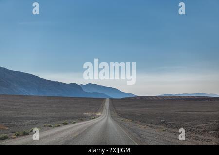 Eine lange Straße zieht sich durch eine Wüstenlandschaft Stockfoto