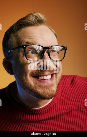 Ein gutaussehender Mann in Brille und rotem Pullover schlägt eine dynamische Pose. Stockfoto
