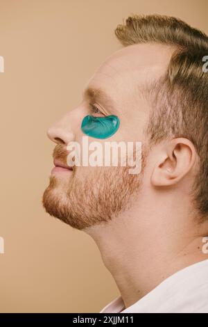Ein gutaussehender Mann in lässiger Kleidung, mit blauem Augenfleck, der sich einer Hautpflegeroutine unterzieht. Stockfoto