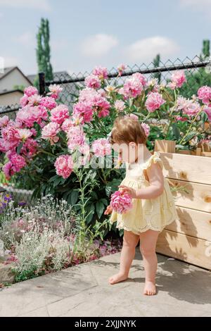 Kleines Mädchen in gelbem Kleid, das Blumen in einem blühenden Garten genießt Stockfoto