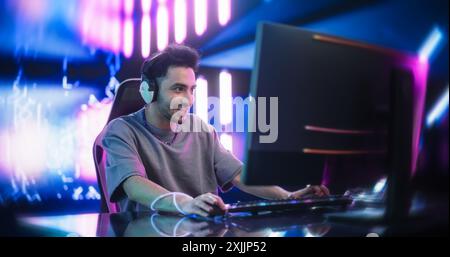 Porträt eines glücklichen jungen Mannes in Kopfhörern, die mit Freunden online auf einem Computer sprechen. Schicker Streamer oder Videospieler spielen Spiele und chatten mit Internet-Followern in einem futuristischen Neon Studio Stockfoto