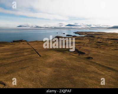 Ein Blick aus der Vogelperspektive auf Islands Küste mit Feldern und schneebedeckten Bergen Stockfoto