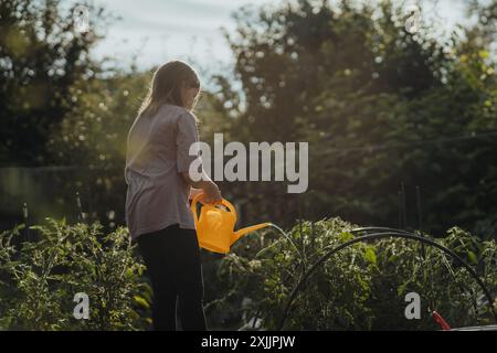 Ein junges Mädchen mit langen Haaren, die Grünpflanzen im Gemüsegarten gießen Stockfoto