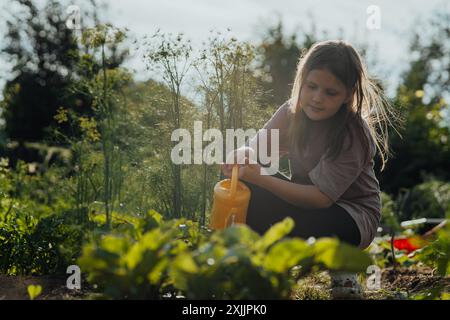 Mädchen bewässern Pflanzen im Garten mit gelber Gießkanne bei Sonnenuntergang Stockfoto