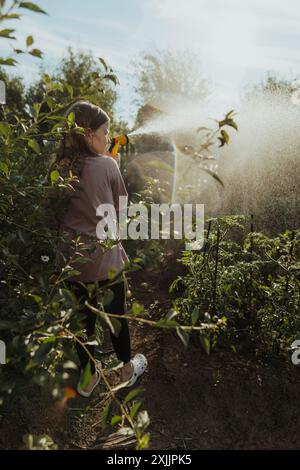 Ein junges Mädchen mit langen Haaren tränkt im Gemüsegarten Grüns Stockfoto