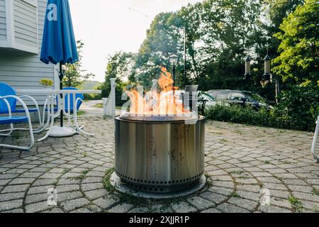 Feuerstelle auf einer Steinterrasse mit blauen Stühlen und einem Tisch Stockfoto