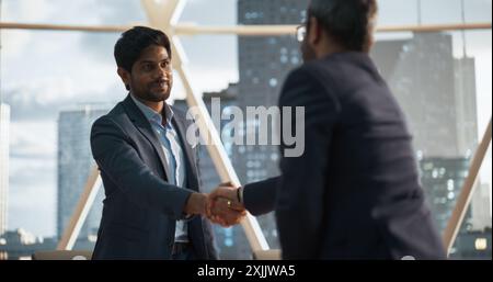 Junge indische Geschäftsleute schließen ein Geschäft in einem Tagungsraum im modernen Corporate Office ab. Zwei Männer in klassischen Anzügen schütteln die Hände und feiern eine erfolgreiche Partnerschaft Stockfoto