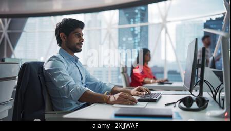 Porträt eines indischen Geschäftsmannes, der an einem Desktop-Computer in einem Fintech Startup Company arbeitet. Finanzanalyst aus Südasien führt Forschung auf dem aufstrebenden asiatischen Technologie-Aktienmarkt durch Stockfoto