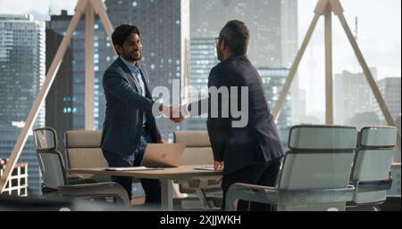 Geschäftspartner aus Südasien erzielen einen erfolgreichen Deal in einem modernen Tagungsraum. Zwei junge indische Geschäftsleute schütteln sich die Hand nach einem positiven Verhandlungsprozess Stockfoto