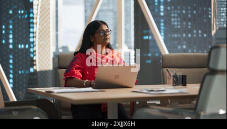 Empowering Portrait einer indischen Geschäftsfrau, die in einem Fintech Startup-Unternehmen an einem Laptop arbeitet. Finanzanalyst führt Forschung an aufstrebenden südasiatischen Aktienmärkten durch Stockfoto