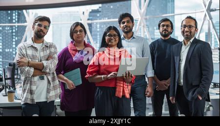 Gruppe von glücklichen, multiethnischen Indianern, weiblichen und männlichen Managern, Spezialisten und Geschäftsleuten, die sich für die Kamera ausgeben und lächeln. Porträt eines selbstbewussten südasiatischen Teamleiters, der an erster Stelle steht Stockfoto