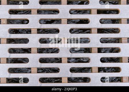 Massiver Metalldeckel, wie ein Mannlochdeckel, über einem kleinen Bach in einer Straße einer Stadt. Klares Wasser fließt in das System. Die Abdeckung dient zum Schutz von p Stockfoto
