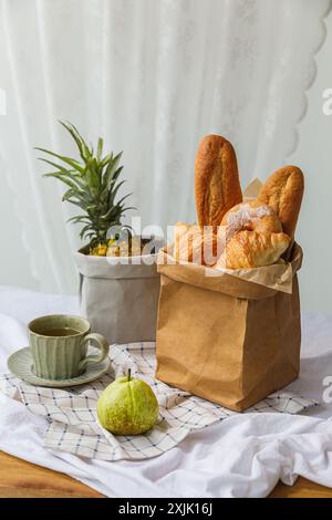 Auf dem mit weißer Tischdecke bedeckten Holztisch befinden sich abwaschbare Papiertüten, Tassen und Guave. In der grau-braunen Kraftpapiertüte sind Kiefer Stockfoto