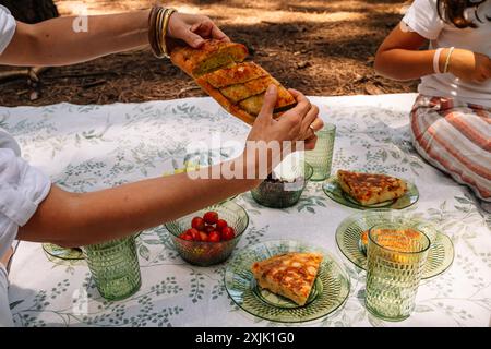 Eine Frau hält ein Stück Brot und legt es auf einen Teller. Auf dem Tisch stehen noch mehrere andere Teller mit Essen, darunter ein Stück Kuchen. Die Registerkarte Stockfoto