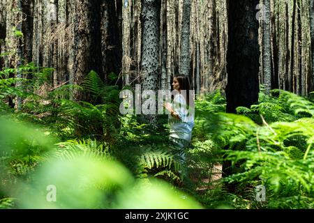 Eine Frau läuft durch einen Wald mit schwarzen und braunen Bäumen. Der Wald ist üppig und grün, und die Frau ist umgeben vom Laub Stockfoto