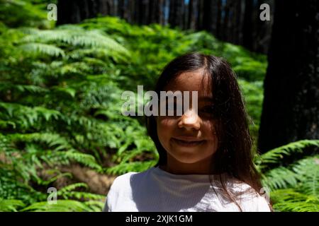 Ein junges Mädchen steht in einem Wald, lächelt und schaut in die Kamera. Konzept von Glück und Abenteuer, da das Mädchen von Natur und h umgeben ist Stockfoto