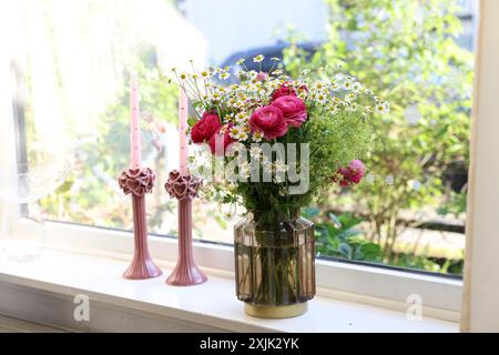 Wunderschöne Ranunkelblumen und Kamillen in Vase auf Fensterbank drinnen Stockfoto