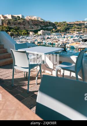 Leeres Café im Freien mit modernen Stühlen und Tisch, mit Blick auf einen Yachthafen voller Boote an einem sonnigen Tag. Stockfoto