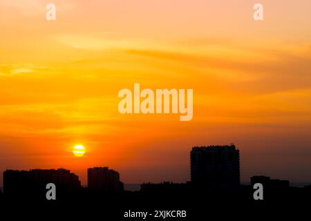 Sonnenaufgang in einem bewölkten Sommerhimmel über der Stadt. Die Sonne bricht durch helle Wolken vor dem Hintergrund von Silhouetten von Gebäuden Stockfoto