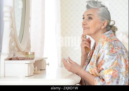 Lächelnde Seniorin, die zu Hause vor dem Spiegel Make-up macht Stockfoto