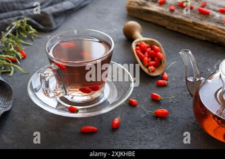 Tasse Kräuter-Goji-Beerentee mit frischen Goji-Beeren auf rustikalem Tisch Stockfoto