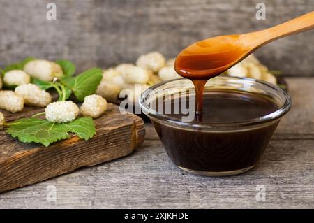 Weiße Maulbeermelasse in Glasschale und Holzlöffel mit frischen Maulbeeren, gesunde Nahrung Stockfoto