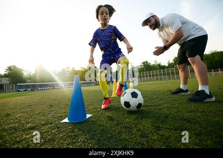 Männlicher Sporttrainer, der jungen Spieler durch Dribbling-Dribbeln führt, ermutigt und kommentiert. Konzentration und Konzentration Stockfoto