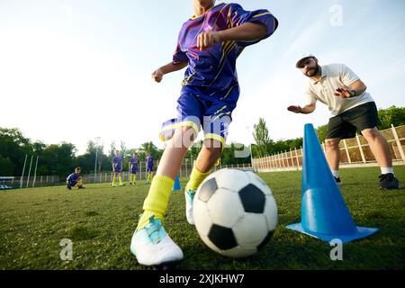 Konzentrieren Sie sich auf die Beine von Jungen, das Kind in Bewegung, das Dribbeln des Fußballballs um die Kegel und das Erhalten der Anleitung durch den Trainer. Stadionspiel im Freien. Stockfoto