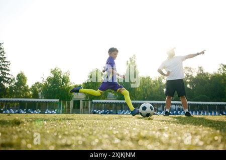 Kleiner Junge, Fußballspieler in Bewegung, der beim Laufen auf einer Datei kräftig tritt, Trainer gibt Orientierung und Kommentare Stockfoto