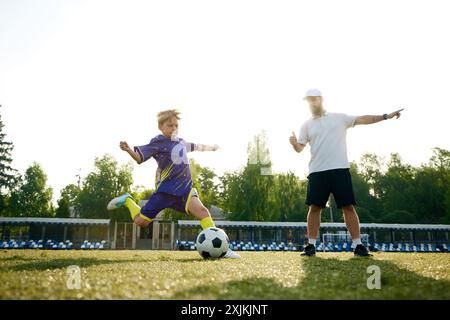 Kleiner Junge, Fußballspieler in Bewegung, der beim Laufen auf einer Datei kräftig tritt, Trainer gibt Orientierung und Kommentare Stockfoto