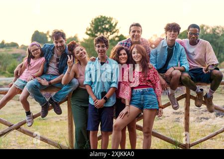 Fröhliche, vielfältige Gruppe von Freunden und Familienmitgliedern, die den Sommer im Freien genießen. Multikulturelle Menschen unterschiedlichen Alters, die in der Natur an Holzzaun kleben, Stockfoto