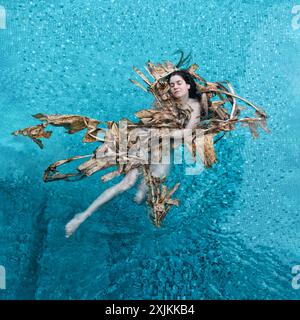 Eine Frau schwimmt friedlich in einem Pool, geschmückt mit getrockneten Bananenblättern. Der Kontrast des leuchtenden blauen Wassers und der natürlichen Erdtöne erzeugt ein s Stockfoto