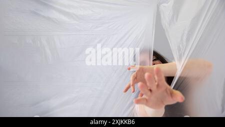 Eine Frau streckt hinter einer durchscheinenden Plastikfolie aus und schafft ein Gefühl von Rätsel und Kampf. Ihre ausgestreckte Hand und teilweise verdeckte fa Stockfoto