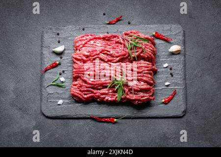 Rohes Hackfleisch auf Steinbrett mit Thymian, schwarzer Paprika und Knoblauch, Metzgerkonzept Stockfoto