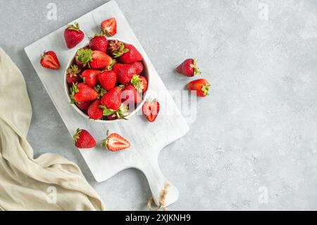 Frische reife Erdbeeren in weißer Schüssel auf weißem Schneidebrett auf rustikalem Tisch, rote Sommerfrüchte Stockfoto