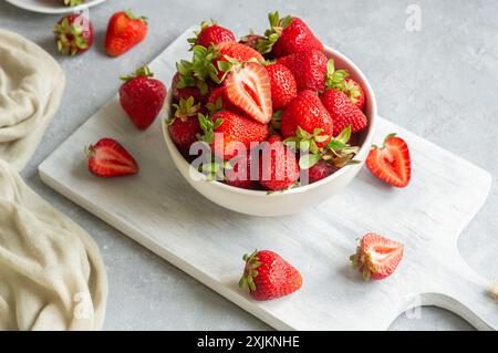 Frische reife Erdbeeren in weißer Schüssel auf weißem Schneidebrett auf rustikalem Tisch, rote Sommerfrüchte Stockfoto