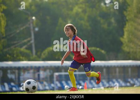 Konzentrierter Junge, Kind in rot und blau Sportswear Dribbeln Ball durch das Feld mit Fokus, Training Fußball Spiel. Stockfoto