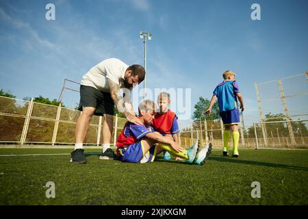 Coach, der Kindern, Jungen, der auf dem Feld sitzt und Schmerzen an den Beinen spürt, während des Spiels verletzt wird. Stockfoto