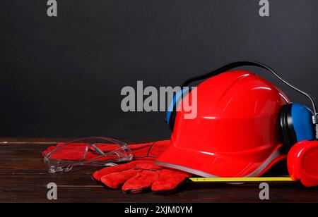 Schutzhelm, Kapselgehörschützer, Schutzhandschuhe und Maßband auf Holzoberfläche vor grauem Hintergrund, Platz für Text Stockfoto