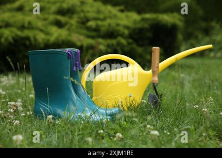 Gummistiefel und Gartenwerkzeuge auf grünem Gras im Freien Stockfoto