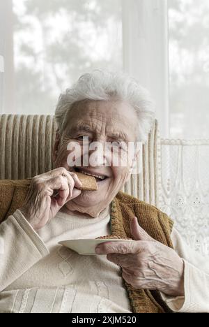 Eine glückliche Seniorin isst zu Hause Kekse Stockfoto