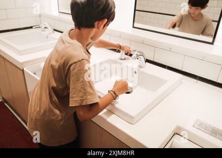 Asiatischer Junge, der seine Hände vor einem Spiegel gewaschen hat, nachdem er die öffentliche Toilette im Einkaufszentrum benutzt hat Stockfoto