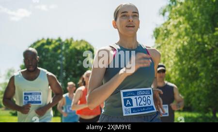 Porträt einer Frau, die in einem Park läuft und an einem Marathon teilnimmt. Starke sportliche Joggingerin, die andere Läufer mit Entschlossenheit für den ersten Platz in der Ziellinie fährt Stockfoto